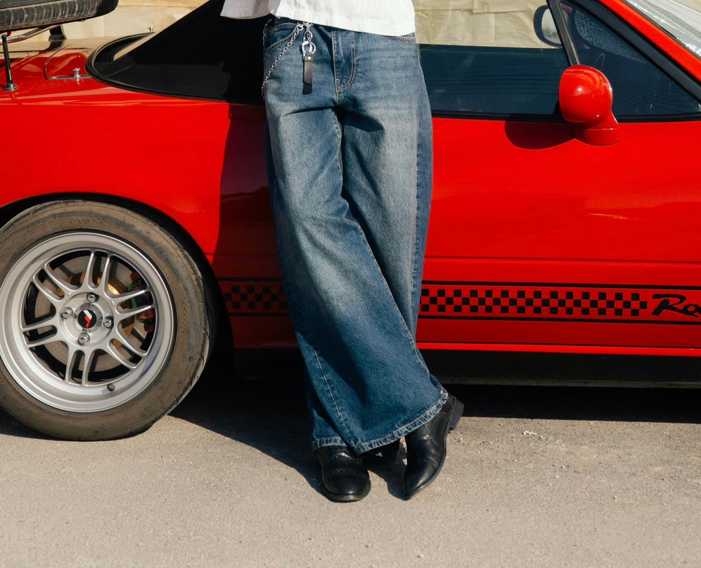 Person in blue jeans standing beside a red vintage car