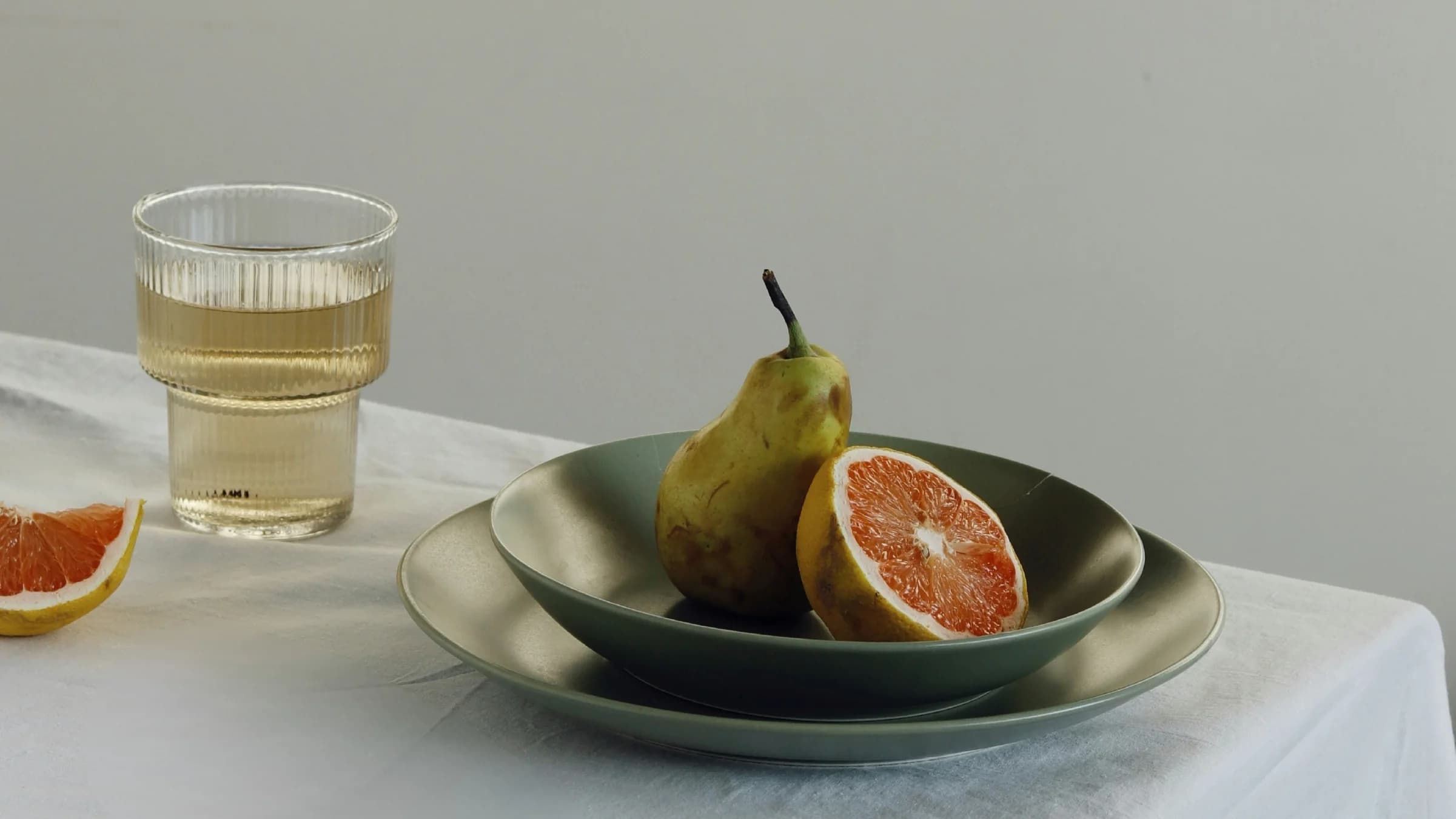 A glass of white wine and a ceramic plate with a pear and halved grapefruit